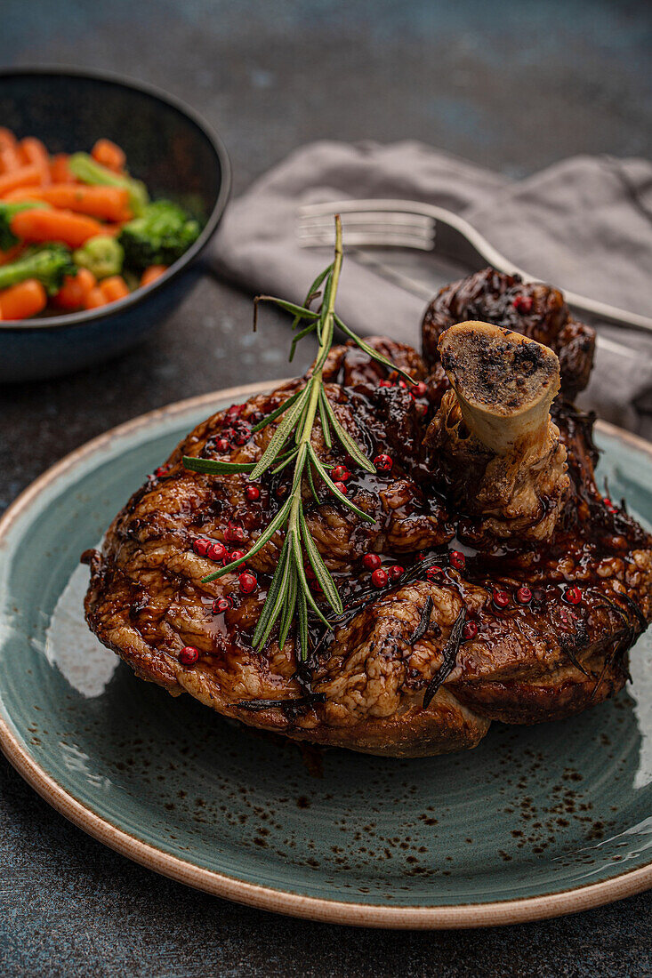 Delicious roasted pork knuckle with glazed brown crispy skin, red pepper berries and rosemary