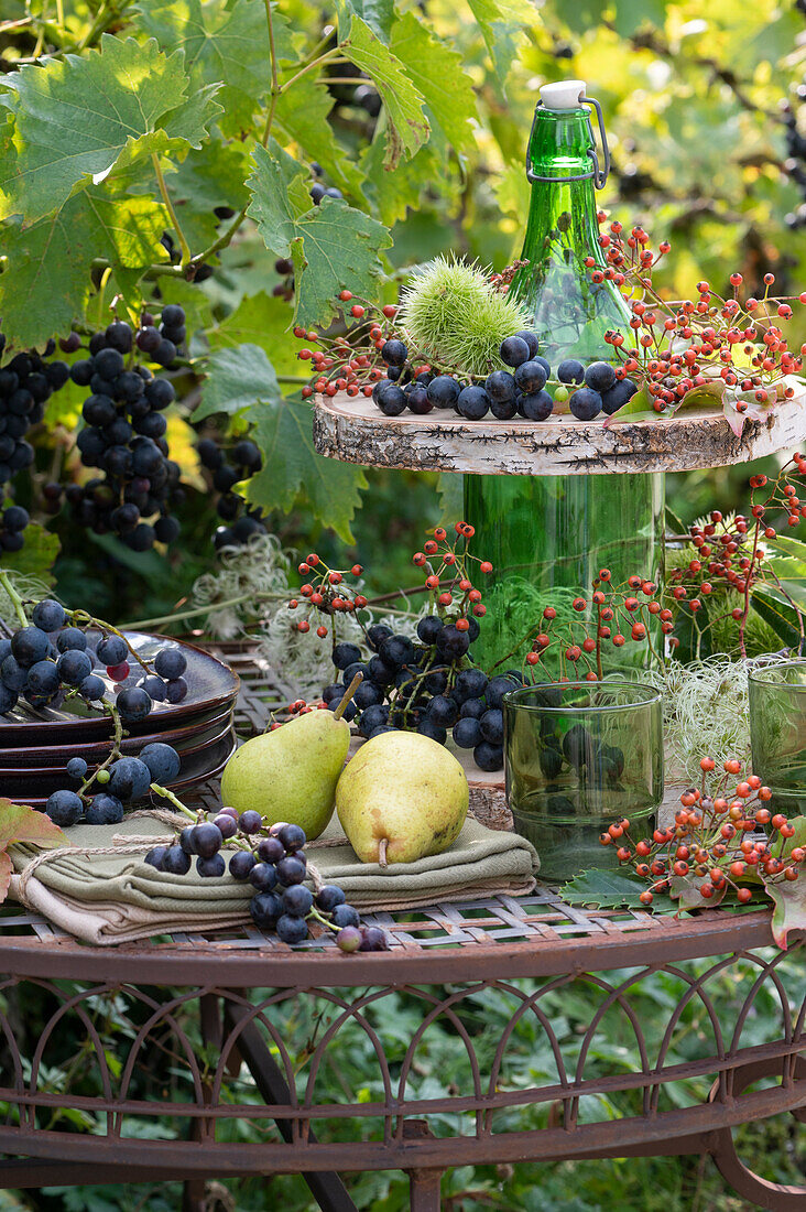 Make your own etagere from a bottle and wooden discs: blue grapes, pears, rose hips and chestnuts in a fruit cover