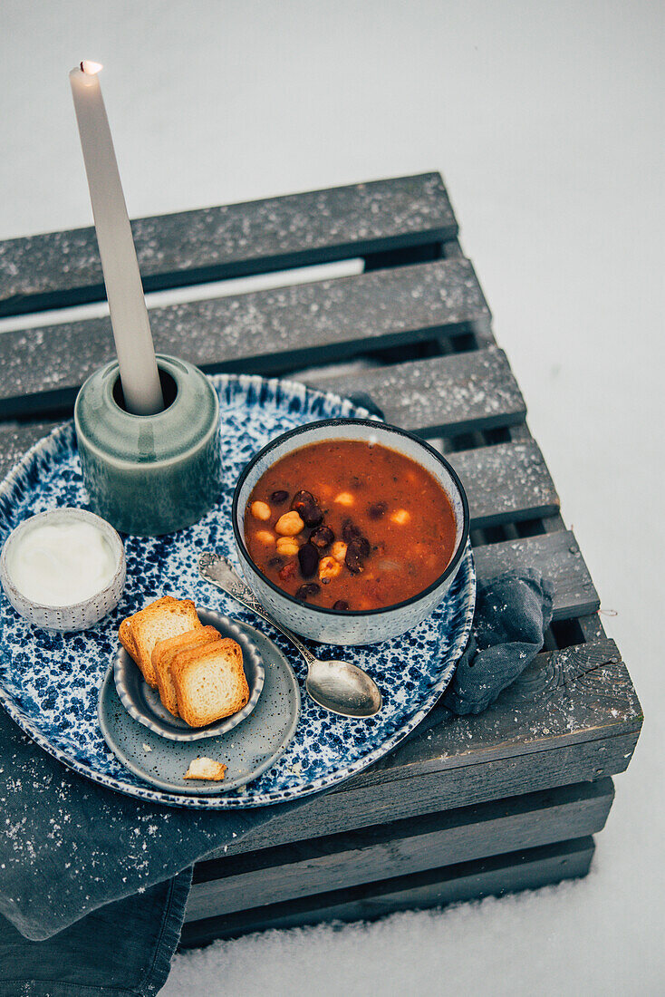 Tomato soup with beans and chickpeas on a wooden box in the snow