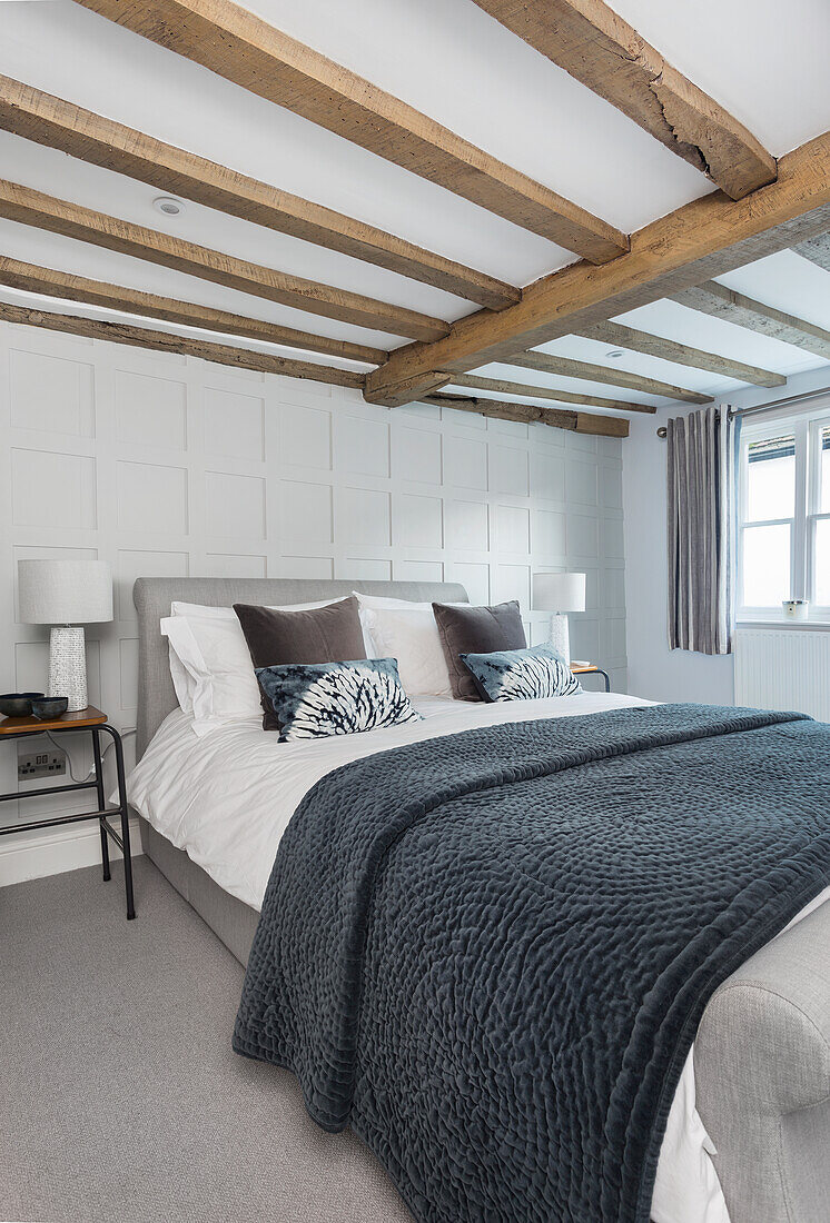 Doppelbett im Gästezimmer mit weiß getäfelter Wand und Holzbalkendecke