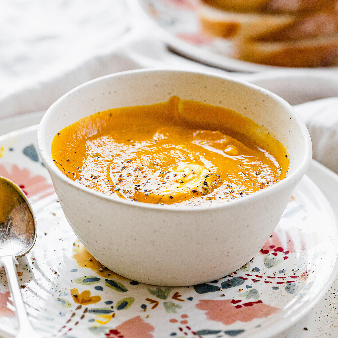 Orange pumpkin soup with a cream and pepper in white stoneware bowl