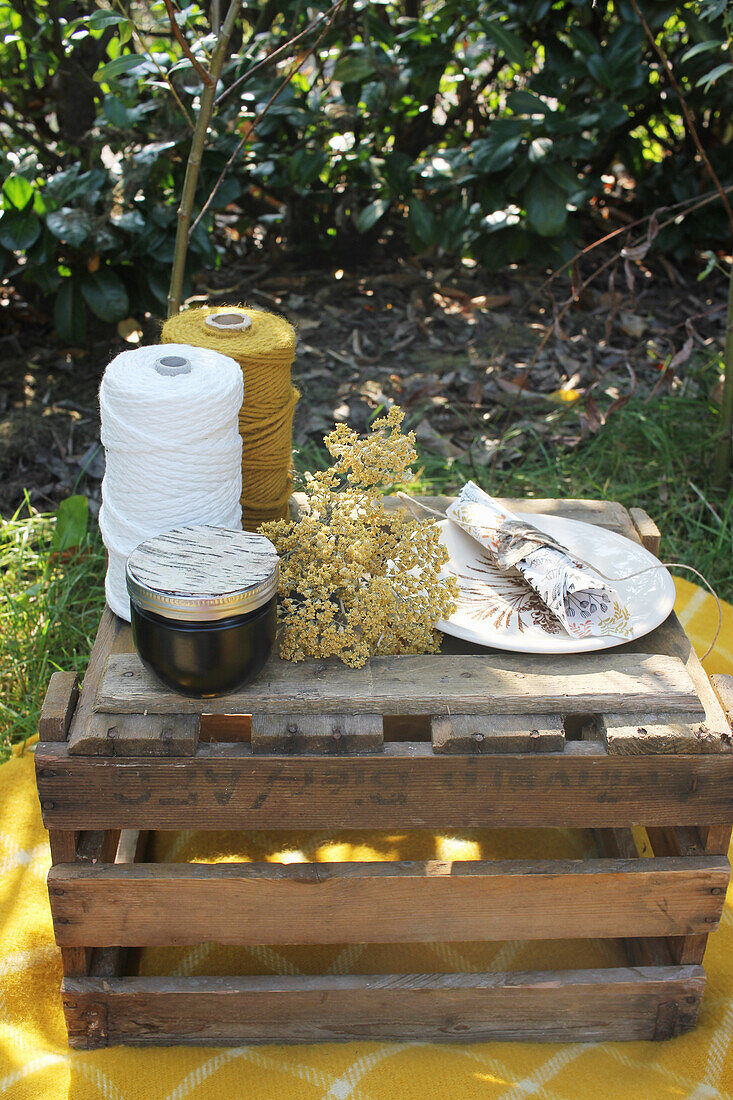 Spools of yarn, jam jar, flower, plate and napkin on wooden box