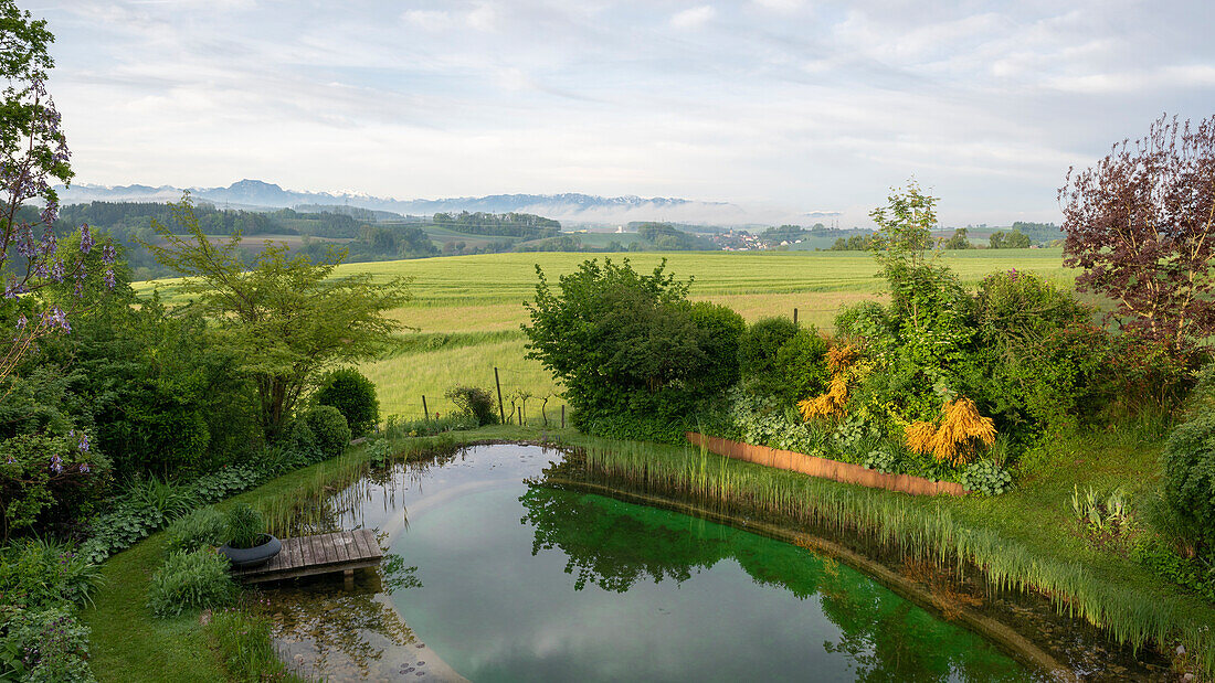 Blick auf Teich mit Holzsteg und Berglandschaft