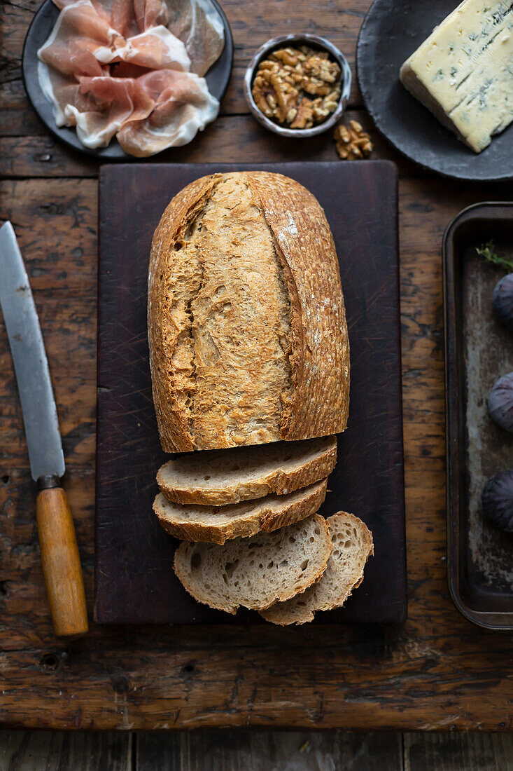 Rustikales Brot, angeschnitten serviert mit Schinken, Nüssen und Käse