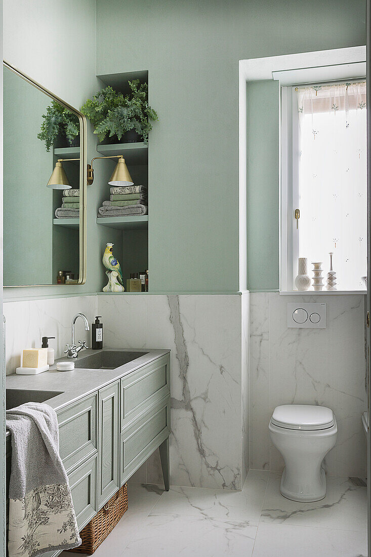 Waschtisch und Toilette im Badezimmer mit Fliesen in Marmoroptik und grünen Wänden
