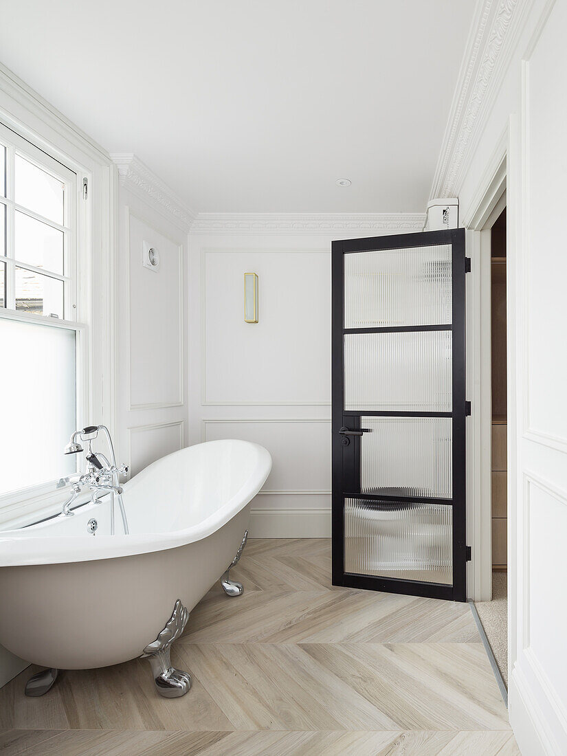 Freestanding bathtub below window in bright bathroom with glass door