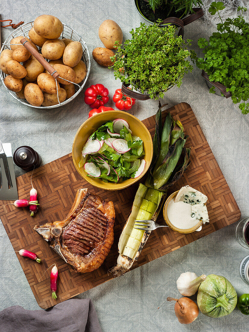 Gegrilltes Steak mit Salat, Lauch und Käsedip, Kartoffeln und Kräuter im Hintergrund