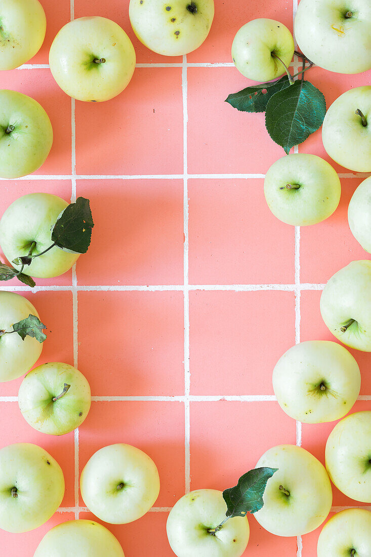 Rahmen aus gelbgrünen Äpfeln auf rosa Fliesen