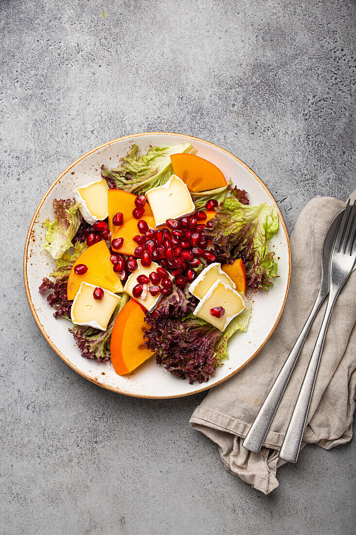 Persimmon salad with brie cheese, fresh salad leaves and pomegranate seeds
