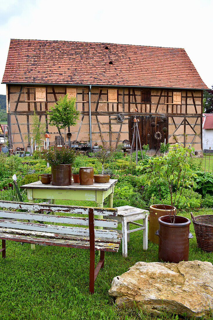 Ländlicher Sitzplatz mit Steinguttöpfen mit Blick auf Bauerngarten und Scheune