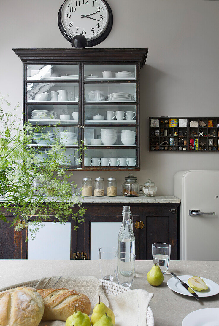 Bread basket, pears and water bottle on a table, in the background china cabinet in a light kitchen