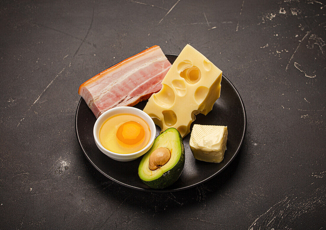 Keto-Hauptnahrungsmittel wie Butter, Olivenöl, Spiegelei, Avocado, Käse, fetter Speck