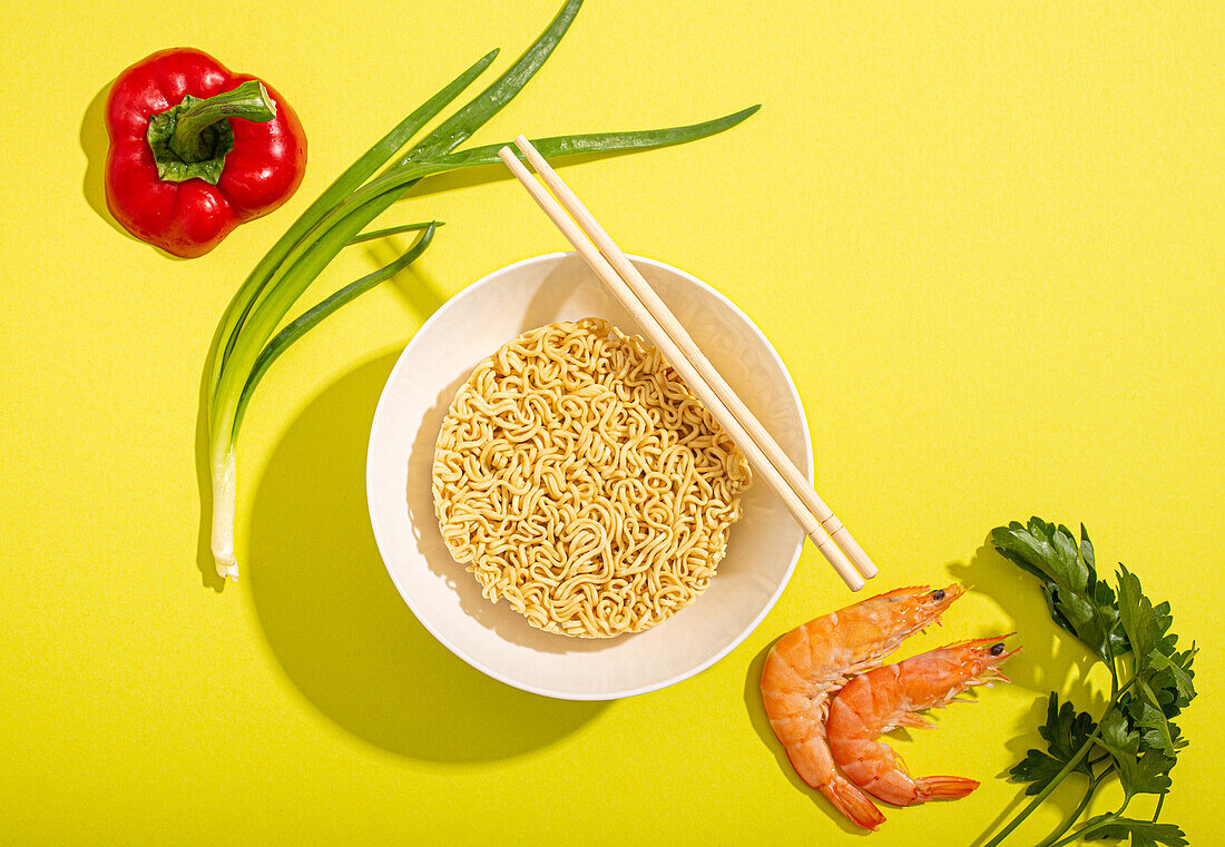 Asian quick noodles, shrimps, vegetables and green onion on bright yellow paper