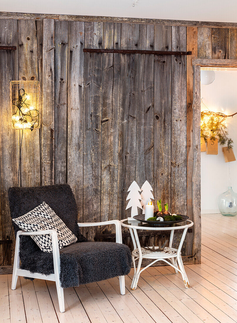 Armchair with cushions, side table, rustic wooden wall and Christmas decorations