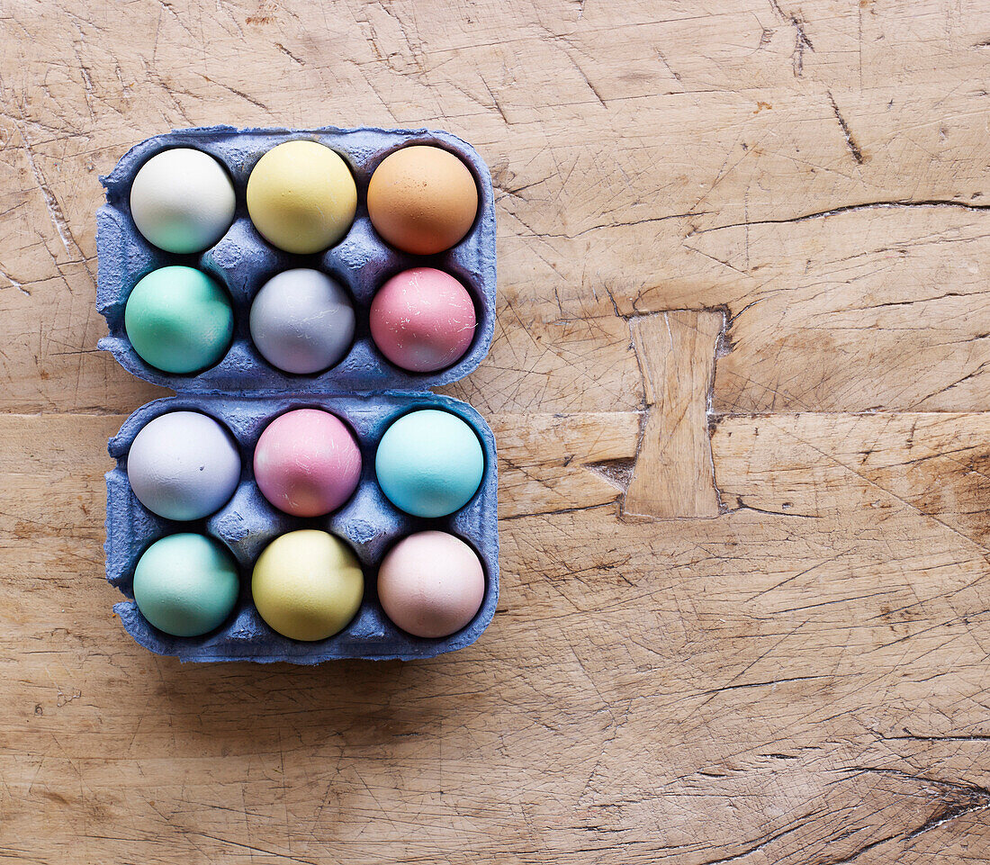 Coloured Easter eggs in egg boxes on a wooden surface