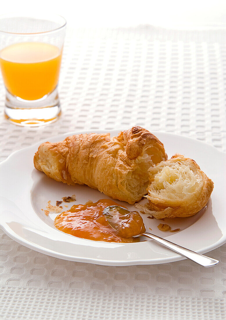 Croissant with apricot jam and glass of fruit juice