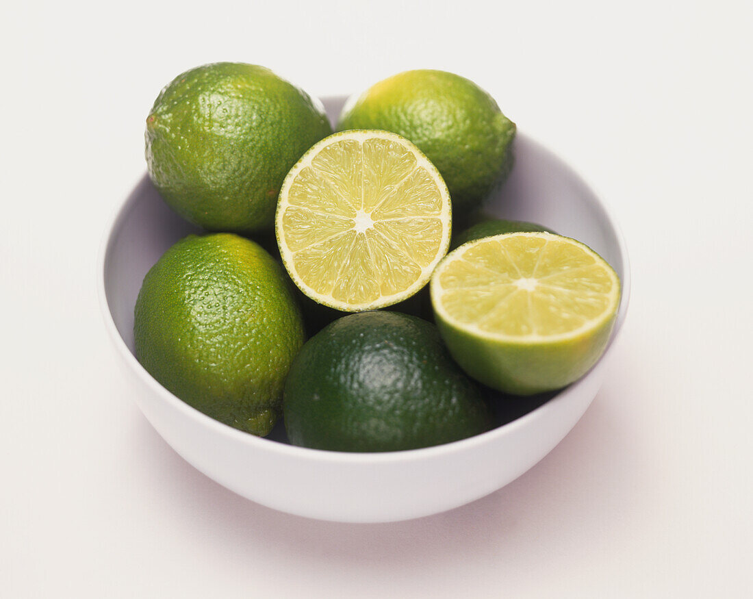 Limes, whole and cut in half, in white ceramic bowl