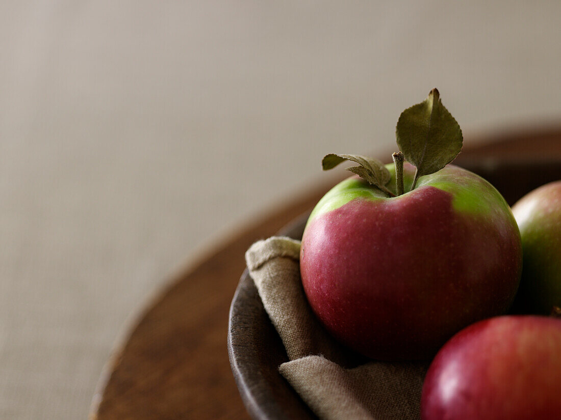 Apples resting on cloth in a wooden bowl on a wooden board