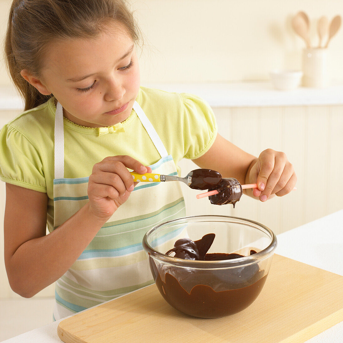 Girl coating banana pieces in melted dark chocolate