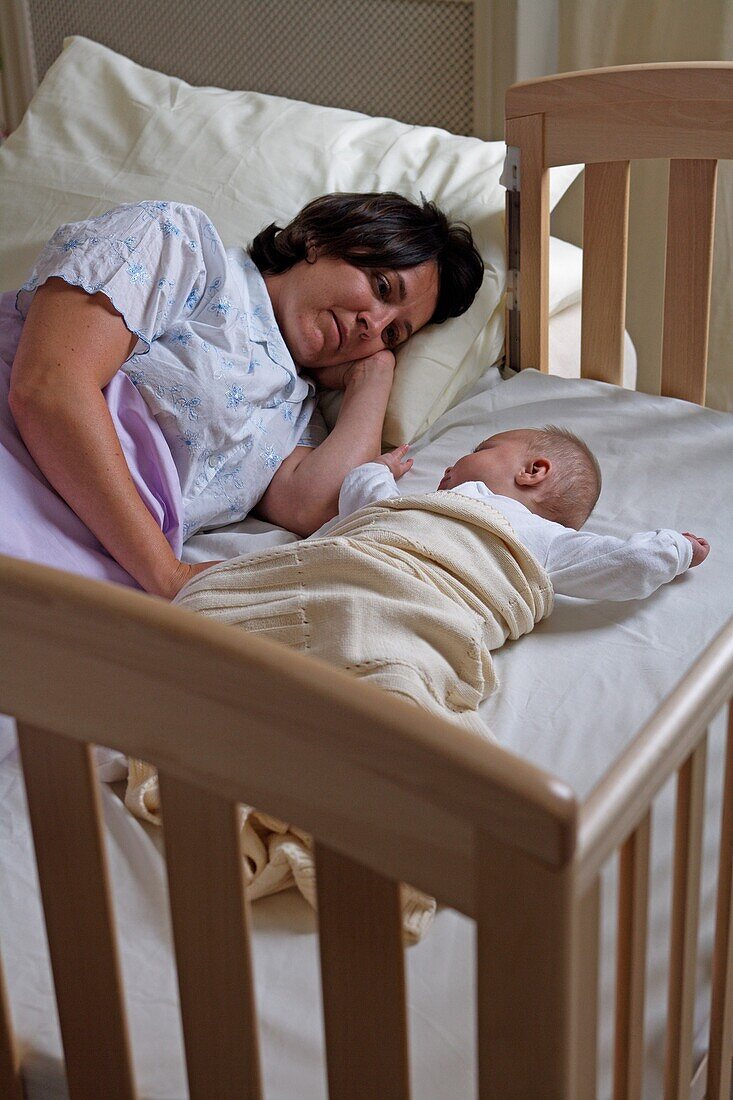 Woman lying in bed next to baby girl in bedside bed