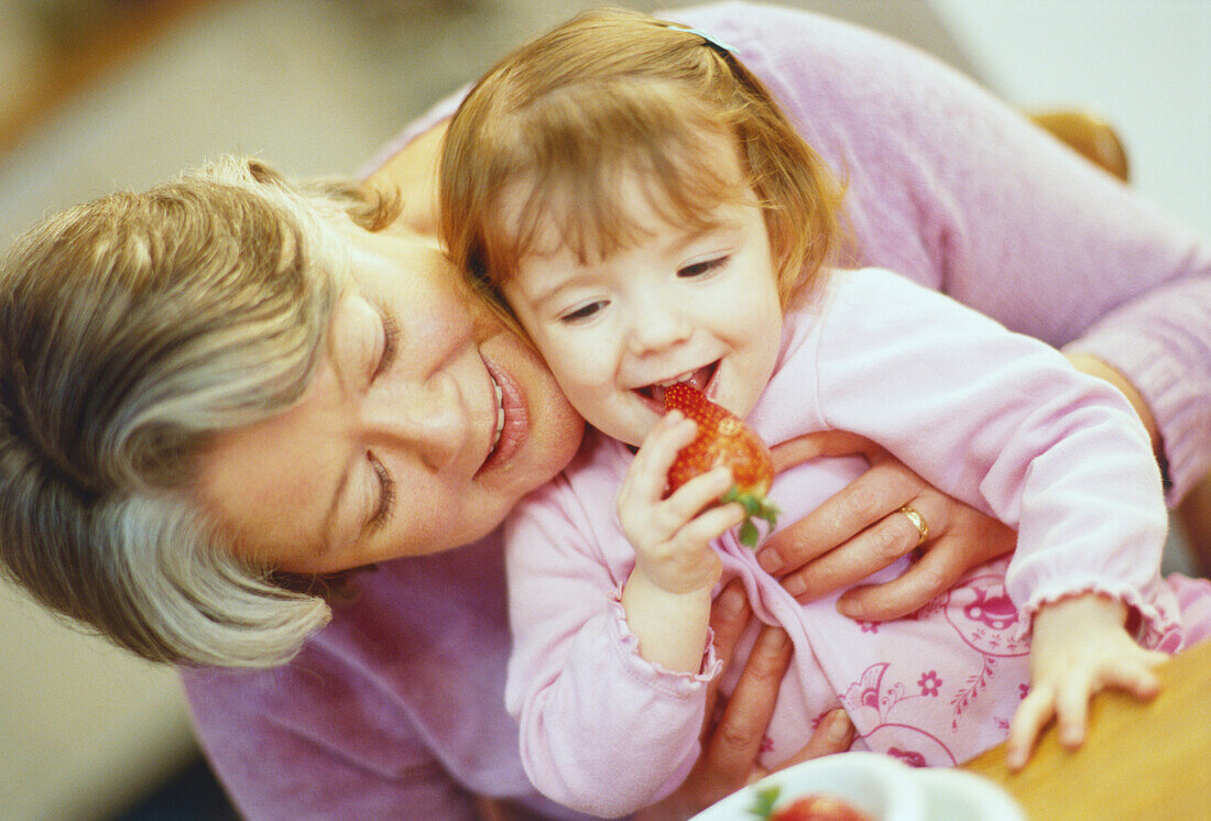 Woman with girl sitting on her lap eating a strawberry