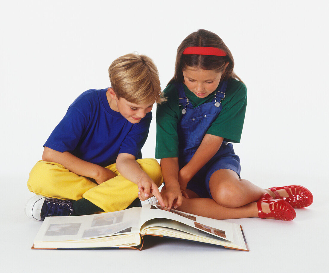 Girl and boy sitting on floor looking at photo album
