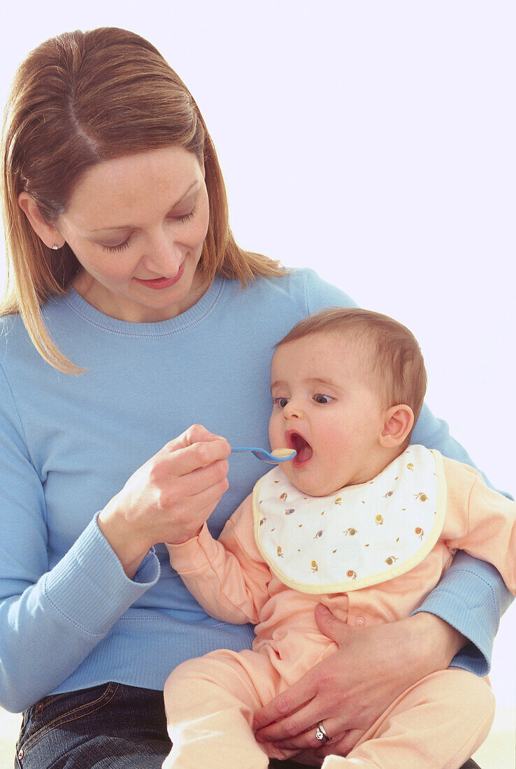 Woman giving food to baby on her lap using plastic spoon
