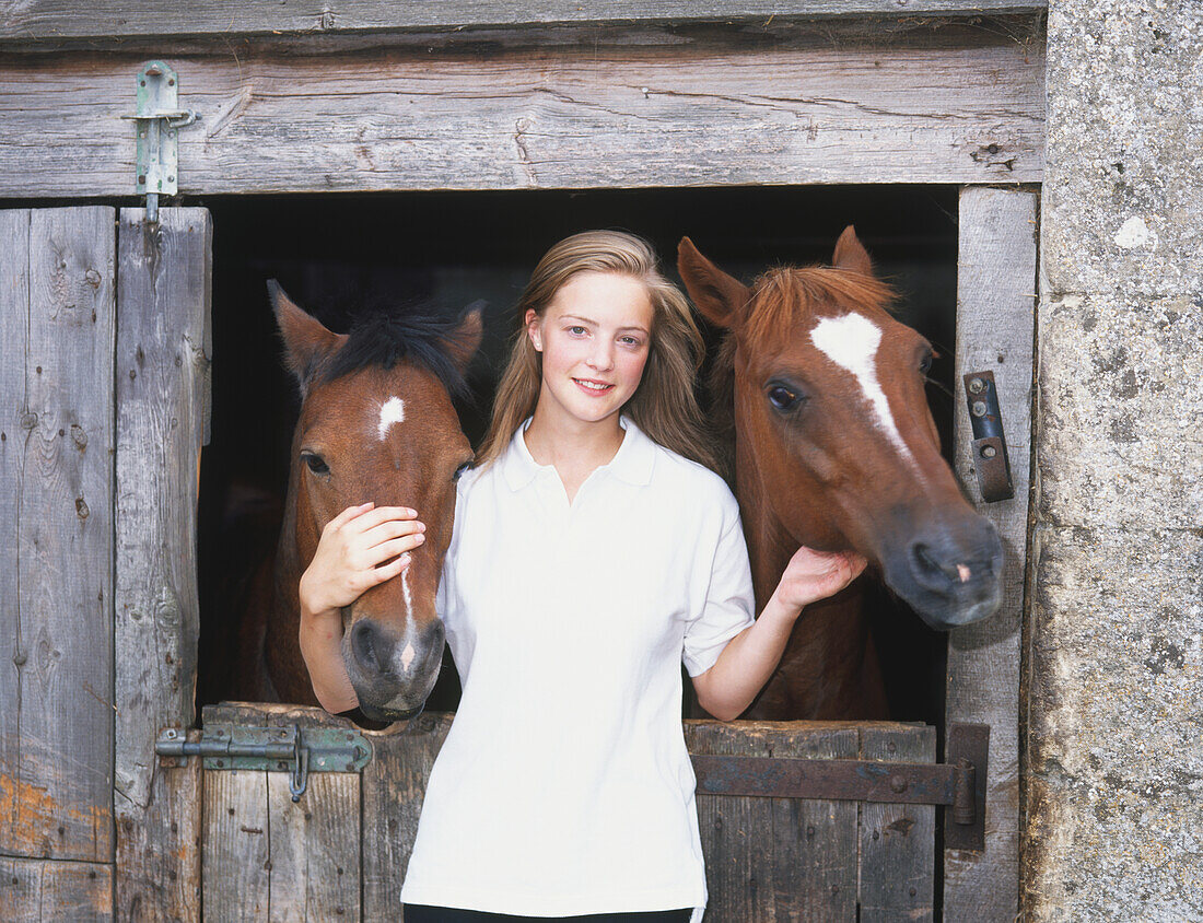 Smiling girl stroking the heads of two horses