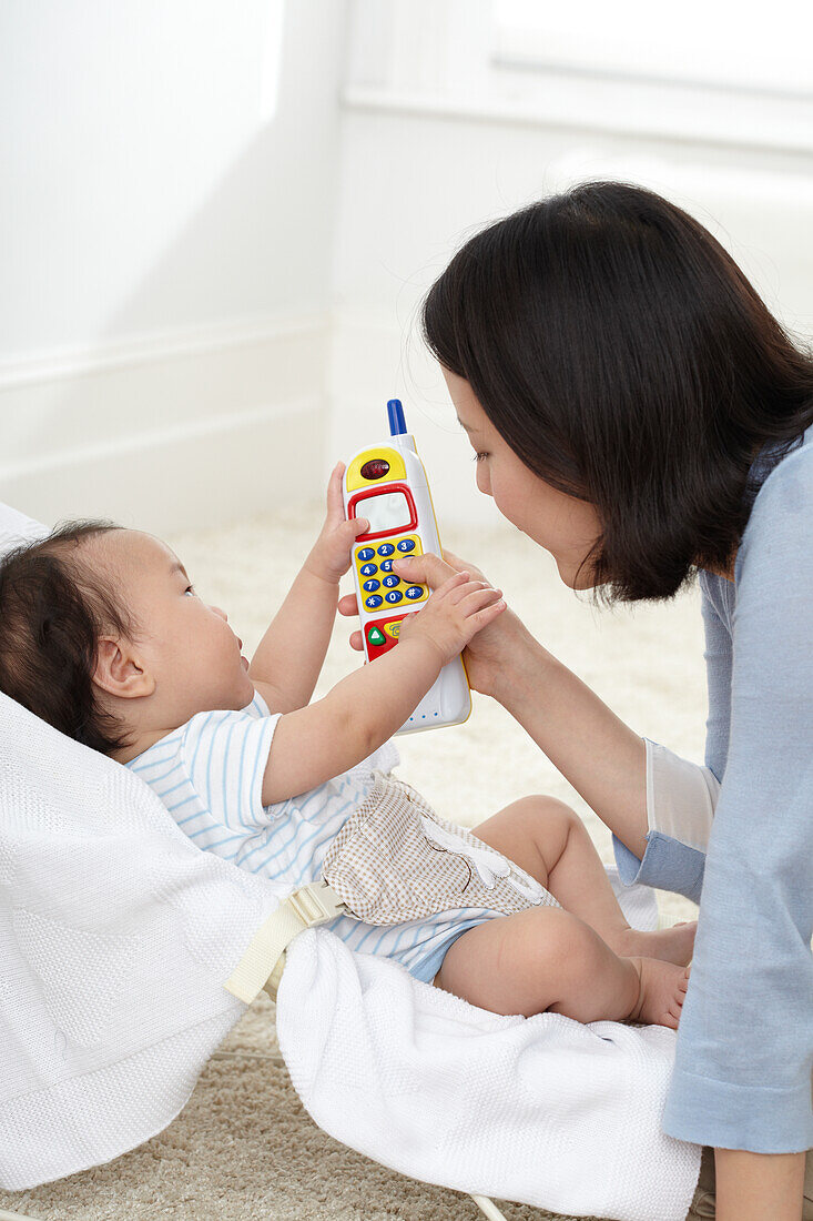 Mother holding toy phone near baby boy in bouncy chair