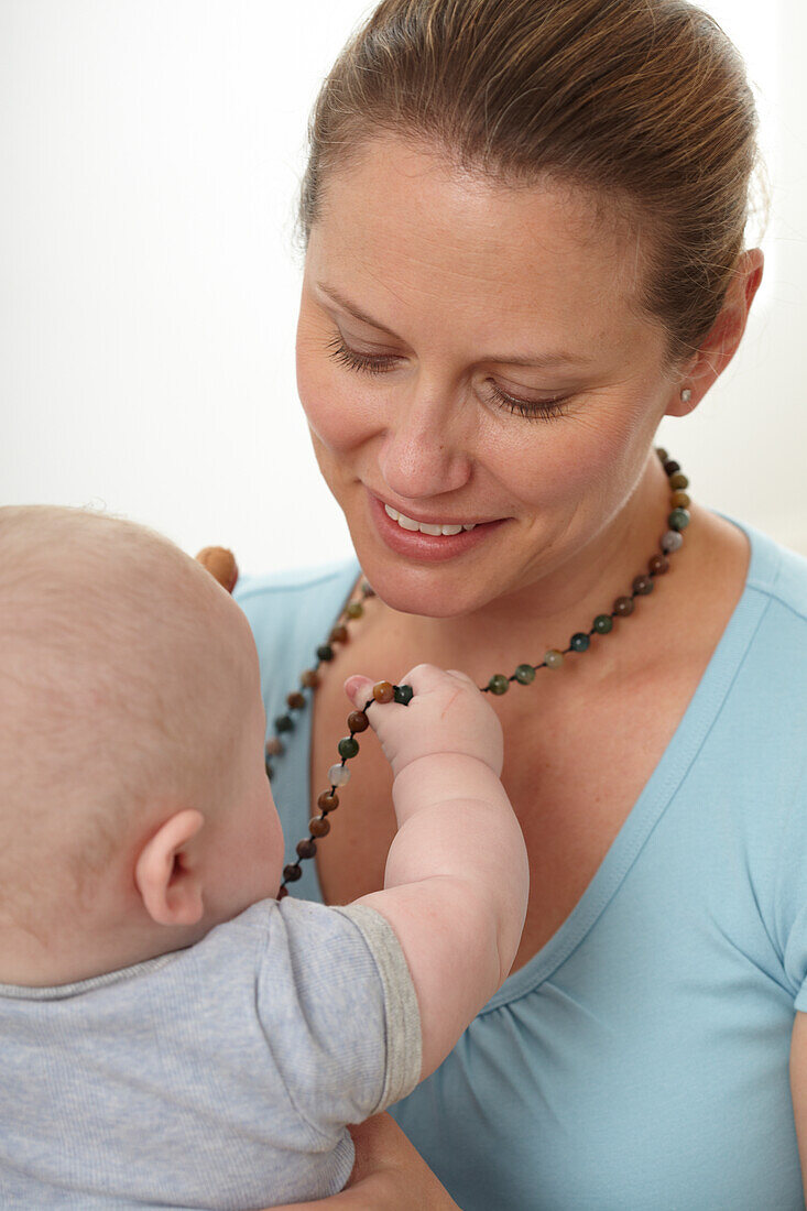 Baby boy holding beads hanging around his mother's neck