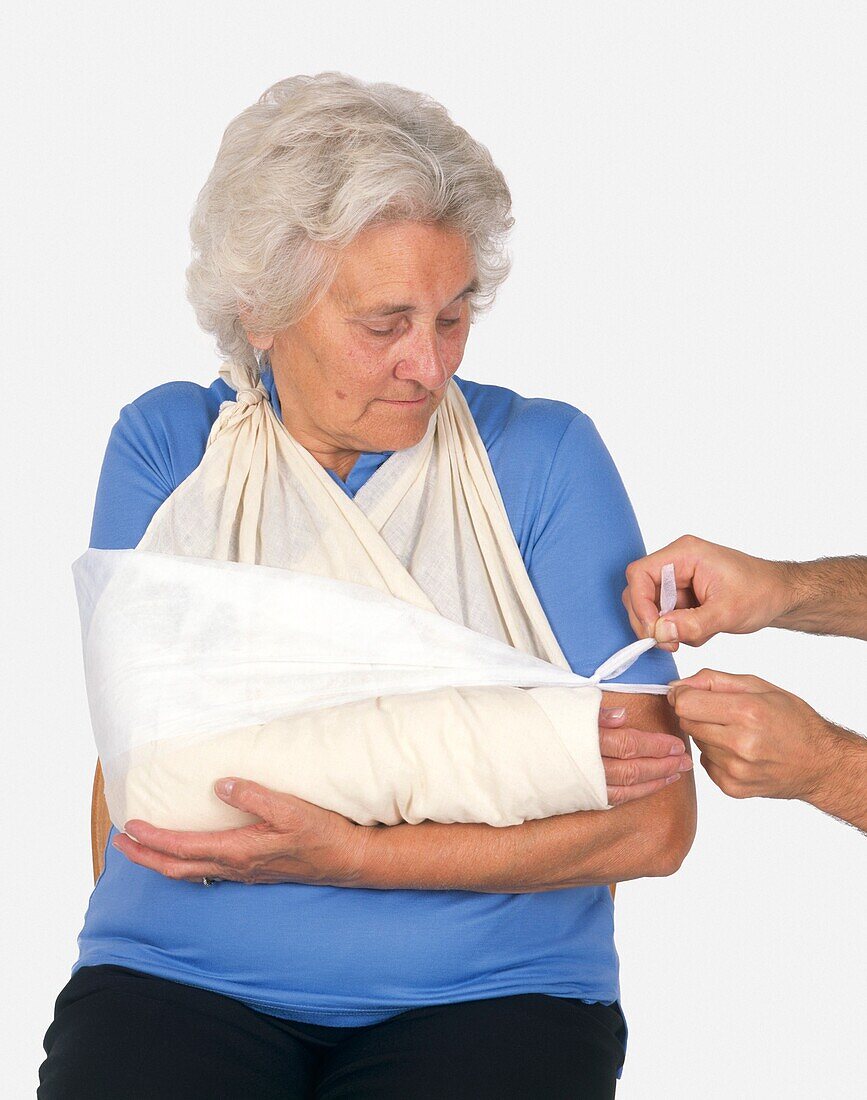 Man's hands tying sling around an elderly woman's arm