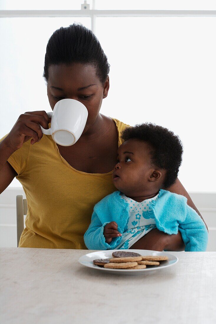 Woman drinking from a mug and holding a baby girl