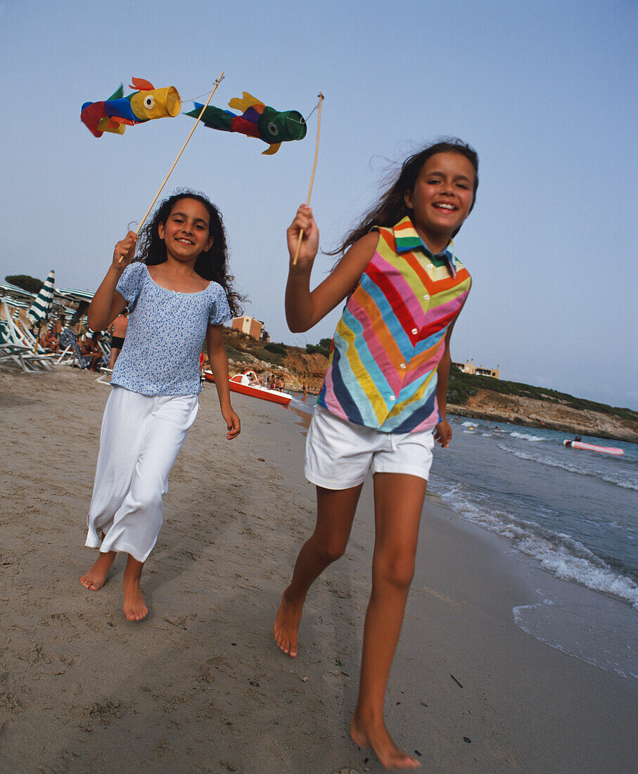 Girls walking on beach holding small paper kites on sticks