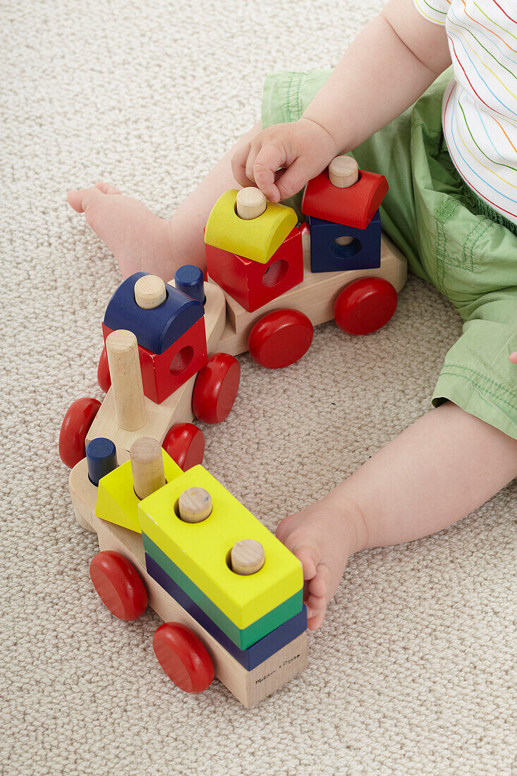 Baby boy playing with wooden shapes on activity toy train