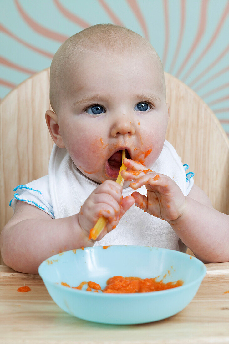 Baby boy in high chair eating pureed food with spoon