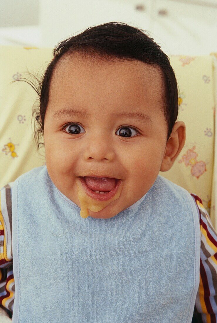 Baby boy with mouth open and food dripping down chin