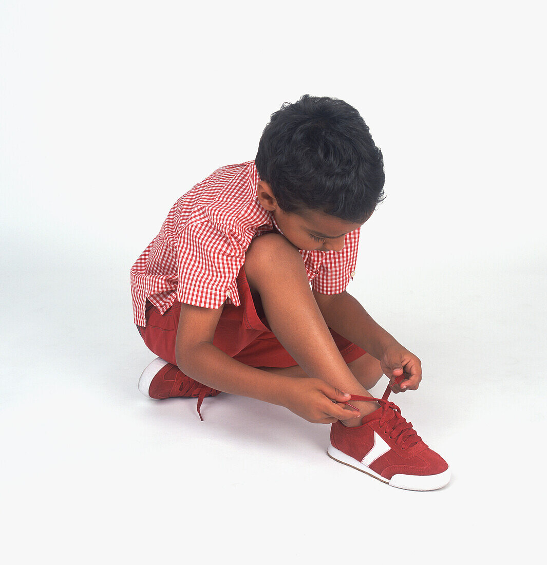 Boy sitting on floor tying shoelace