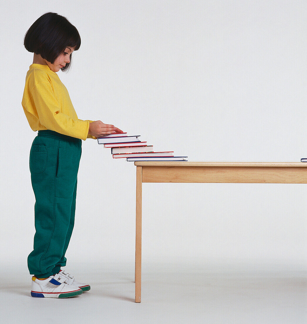 Girl stacking books up on the edge of a table
