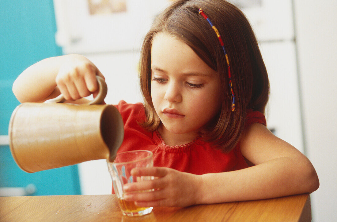 Young girl pouring water into a glass from a jug