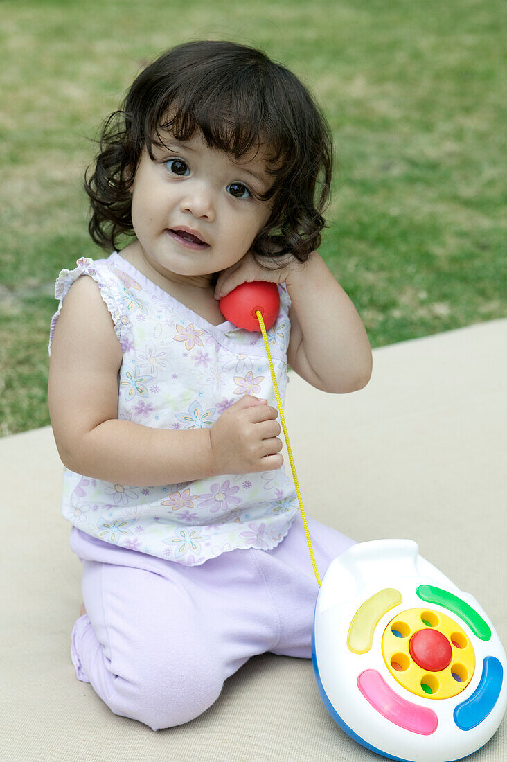 Baby girl in garden playing with plastic toy telephone