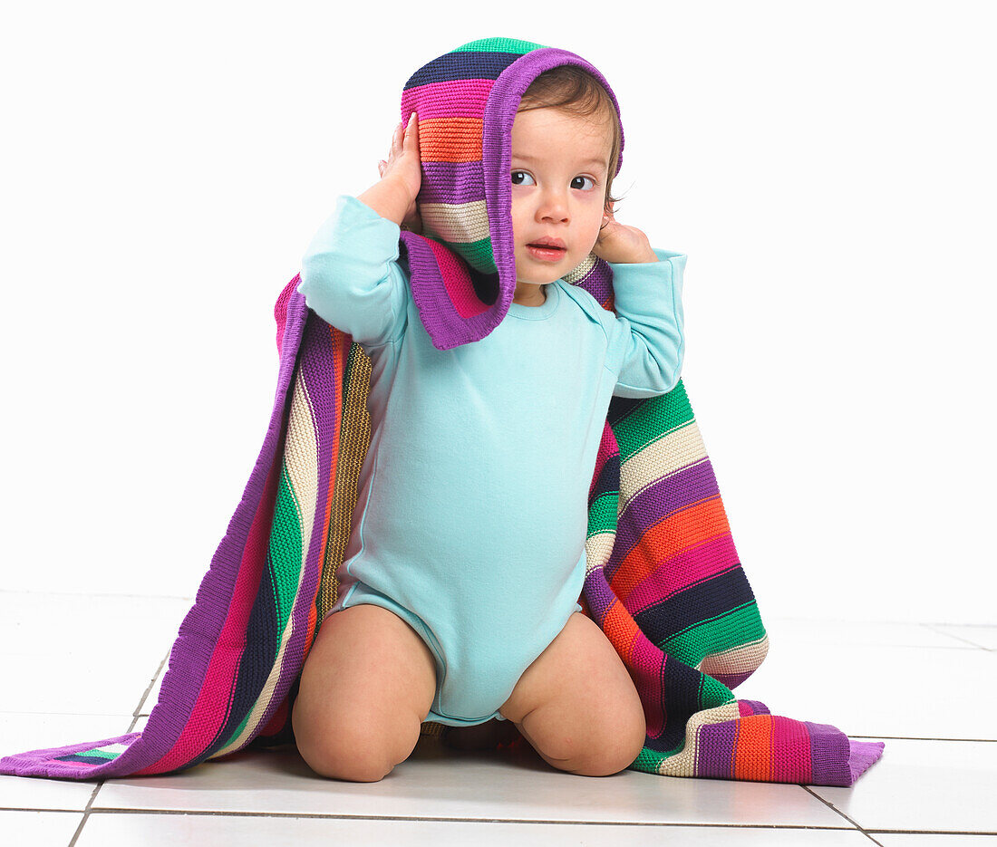 Toddler boy with colourful striped blanket on his head