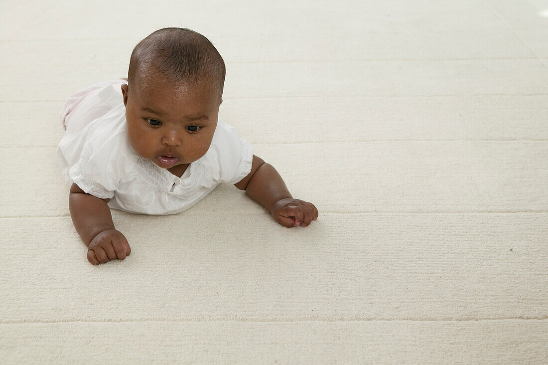 Baby girl in white top and trousers crawling on the floor