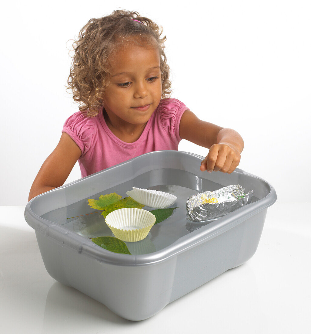Girl looking at objects floating in washing-up bowl
