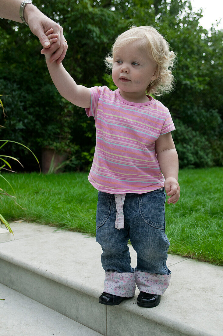 Baby girl walking in garden with woman holding her hand