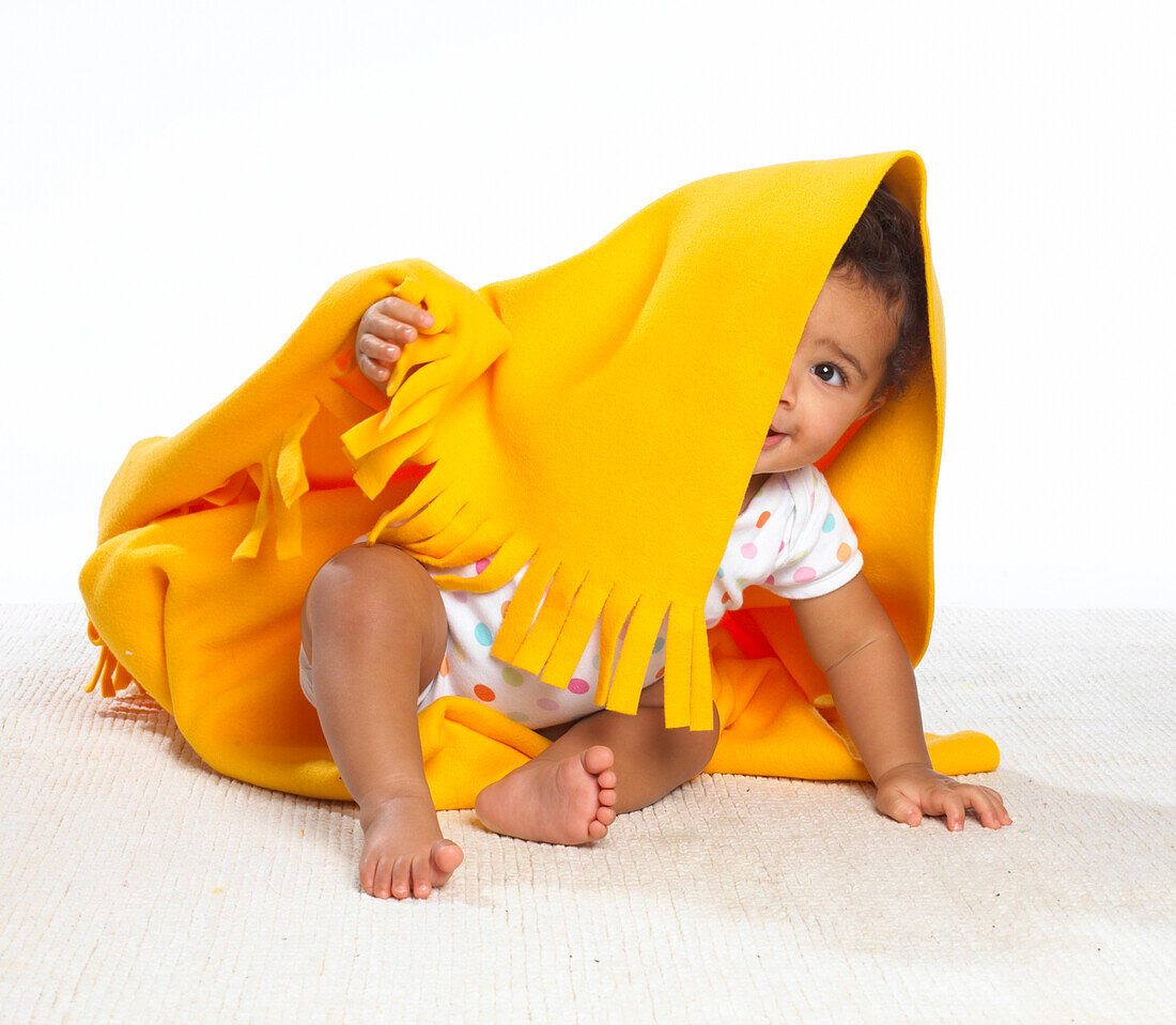 Baby girl peeping out from under yellow blanket