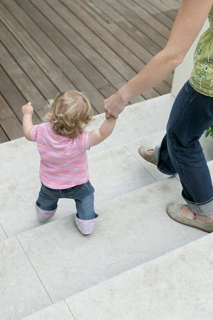Baby girl walking on patio steps with woman holding her hand