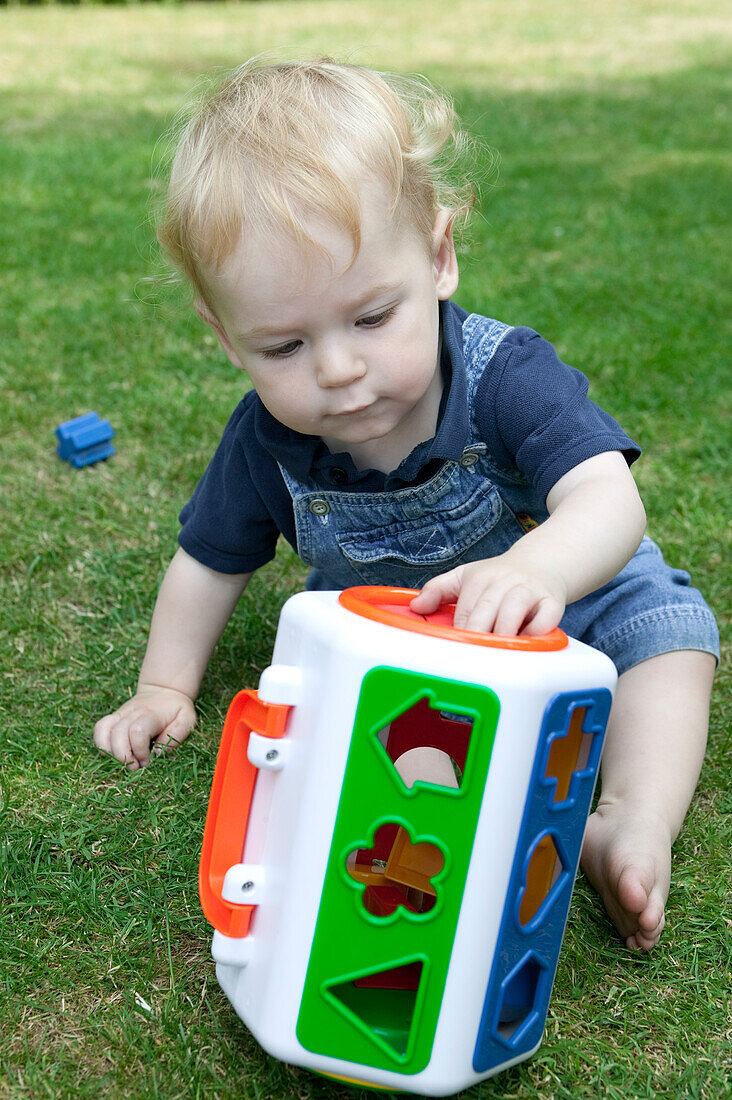 Baby boy playing with shape sorting toy in a garden