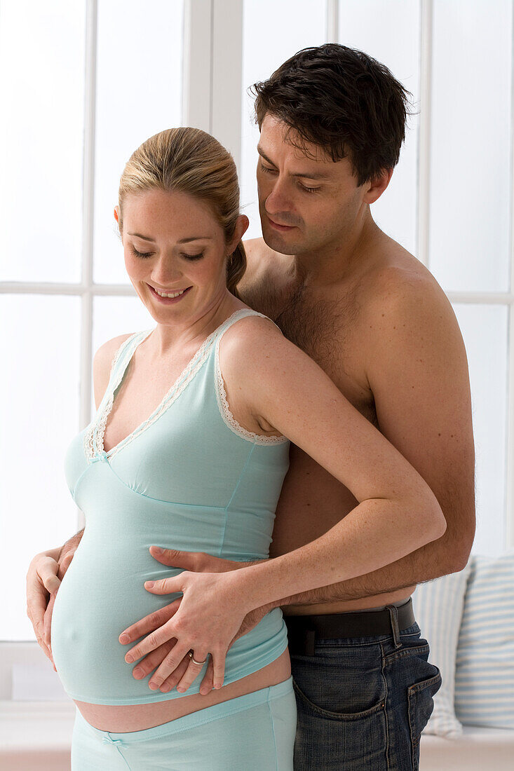 Man standing behind woman with his hands on her bump
