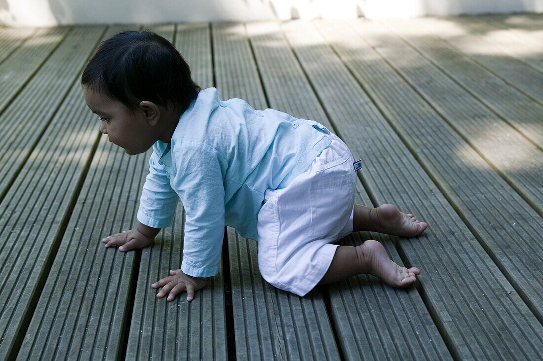 Baby girl crawling on patio decking