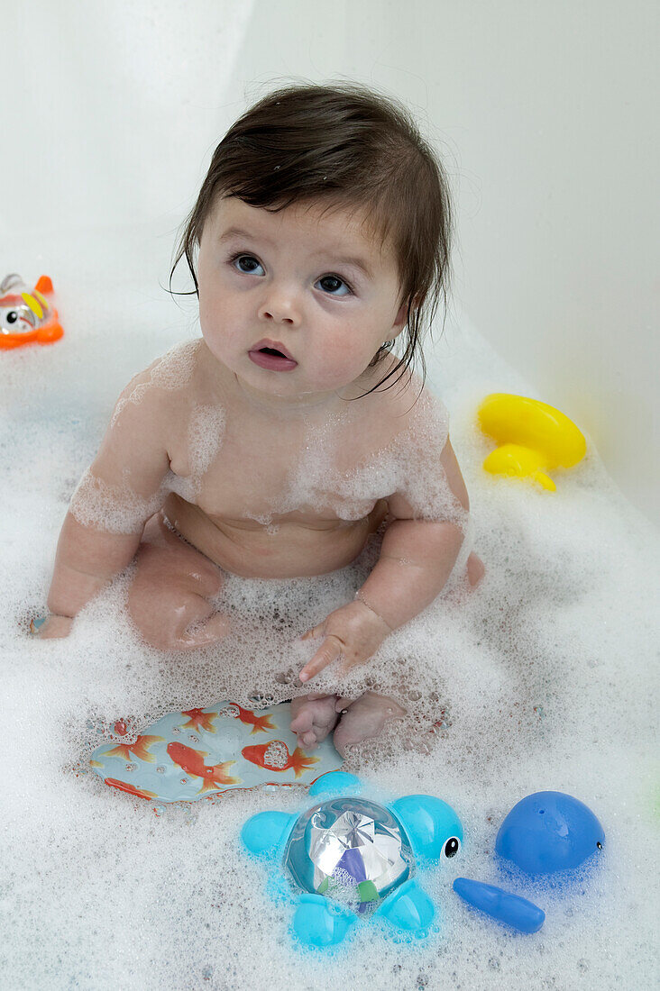 Baby girl sitting in bath with toys